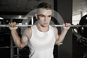 Confident muscular man trainings squats with barbells overhead in gym photo