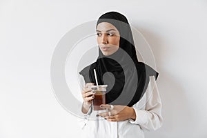 A confident muslim woman in hijab holding a plastic glass and looking to the side
