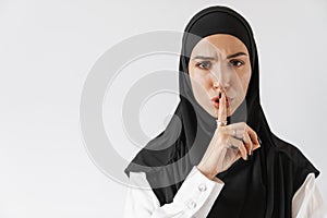 A confident muslim woman in hijab showing a silence gesture and wrinkling her forehead