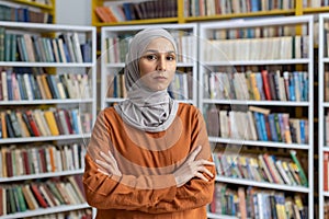 Confident Muslim woman standing in a library with arms crossed