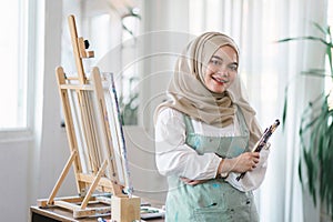 Confident muslim young female artist painting on canvas at home. Hobby and leisure concept.