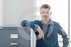 Confident office worker smiling and leaning on the filing cabinet