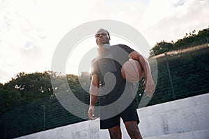 Confident person. Young black man is with basketball ball outdoors