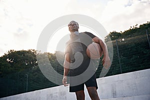 Confident person. Young black man is with basketball ball outdoors