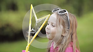 Confident playful little cute girl blowing huge air soap bubble blower medium close-up
