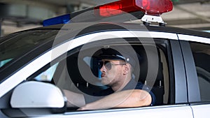 Confident policeman in sunglasses sitting in car, ready for area patrolling duty