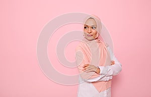 Confident portrait of Arabic Muslim beautiful woman with attractive gaze and covered head with pink hijab, stands three quarters