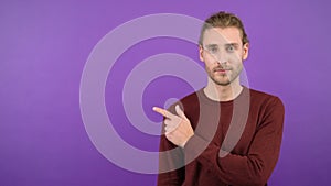 Confident portrait of calm young long-haired man pointing sideways at space on isolated purple background. 4K