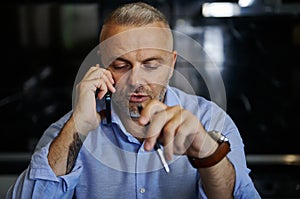 Confident portrait of handsome middle aged man talking on mobile phone, holding a pen in his hand