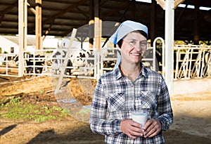 Confident female milker approvingly demonstrating milk on dairy farm