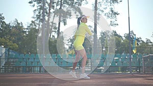 Confident pretty girl in a sportswear holds a tennis racket while standing on the tennis court oudddoors. Young tennis