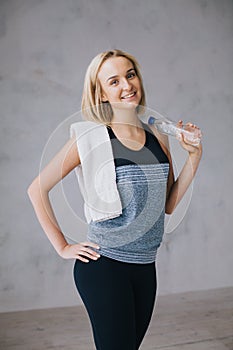 Confident pretty young sportswoman standing with bottle of water and white towel