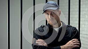 Confident prison security guard looking to camera standing near cell, profession