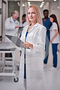 Confident Professional Female Doctor Posing At Camera Holding Clipboard in Hands