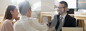 Confident realtor greeting clients young married couple in office