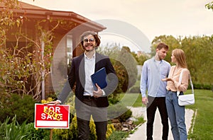 Confident realtor and happy young couple near beautiful country house outside