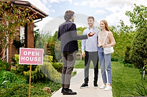 Confident realtor showing house for sale to newlywed young couple, outdoors