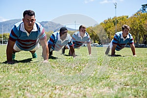 Confident rugby players doing push up at field
