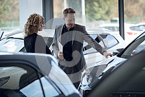 Confident salesman showing car to customer in showroom