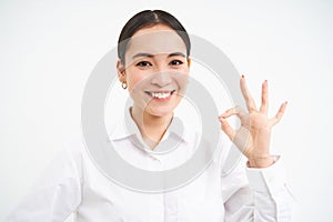 Confident saleswoman, team leader shows okay, ok sign in approval, say yes, recommends something, stands over white