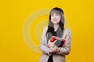 Confident satisfied young business woman in a gray jacket with pair of notebooks