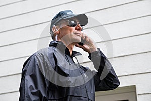 Confident Security Guard Listening To Earpiece Against Building