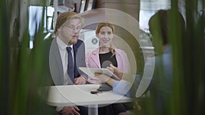 Confident seller woman in formal suit shows information to man and woman customers on her tablet in modern motor show