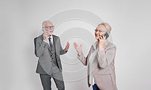 Confident senior business partners talking over mobile phones while standing over white background