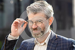 Confident senior businessman adjusting glasses outside modern office building