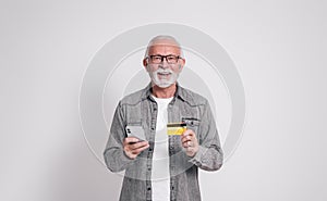 Confident senior businessman with credit card and smart phone smiling at camera on white background