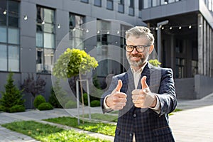 Confident senior businessman giving thumbs up outside corporate building