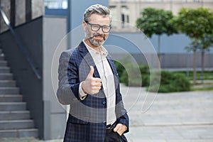 Confident senior businessman giving thumbs up outside modern office building