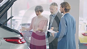 Confident senior Caucasian woman discussing car purchase with handsome man in dealership. Portrait of wealthy couple