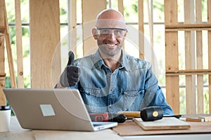 Confident senior craftsman carpenter wearing goggle and glove in the wood workplace. Looking forward and thumb up. There are