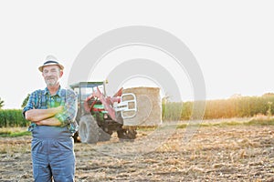 Confident senior farmer standing with arms crossed against tractor in field photo