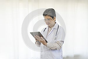 Confident senior female doctor using tablet computer standing in clinic.