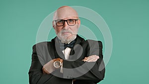 Confident Senior Man Putting on Glasses with Crossed Arms on Teal Background