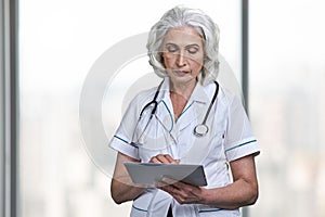 Confident senior woman doctor with stethoscope using digital tablet pc.