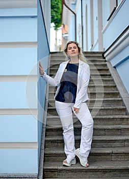 Confident and serene Caucasian woman in a white suit  standing on the stairs