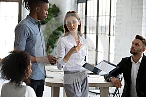 Confident serious businesswoman in suit standing telling diverse employees.