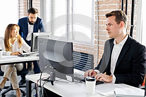 confident and serious caucasian male office worker sits at computer working