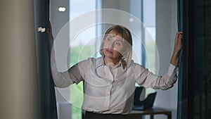 Confident serious female CEO opening curtains in new office looking around walking to table in slow motion. Portrait of