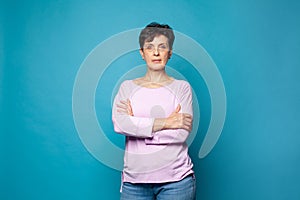 Confident serious mature woman with crossed arms standing against blue studio wall background