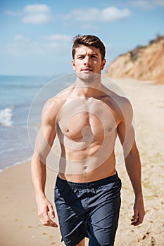 Confident shirtless young man walking along the beach