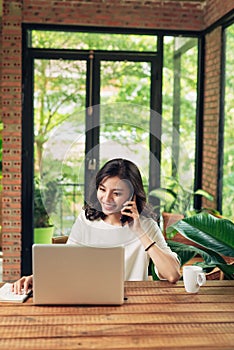 Confident smiling asian woman using phone and laptop