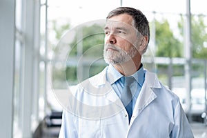 Confident smiling doctor posing in the hospital with medical team working on the background.