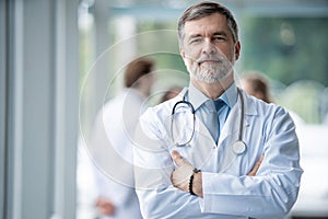 Confident smiling doctor posing in the hospital with medical team working on the background.