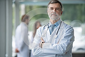 Confident smiling doctor posing in the hospital with medical team working on the background.