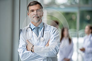 Confident smiling doctor posing in the hospital with medical team working on the background.