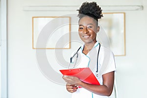 Confident smiling doctor posing and looking at camera with clipboard in her hands. Friendly African American female doctor smiling